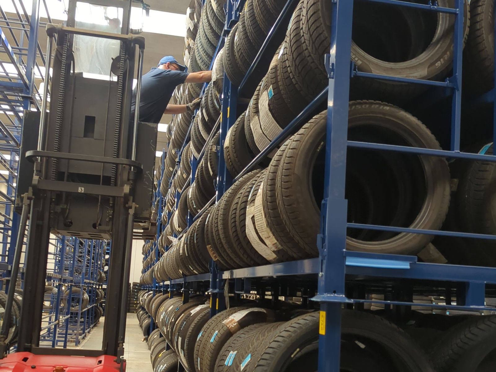 Corsia del magazzino Tyre-Hotel con pneumatici stoccati ed etichettati su scaffalature, operatore al lavoro